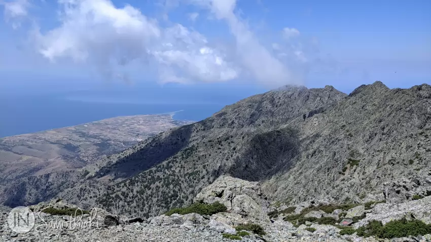 A red arrow on a rock points the way toward Chora. In the distance, you can see Kamariotissa Bay.