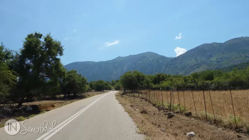 The road winds through the wheat fields towards the towering mountains in the background.